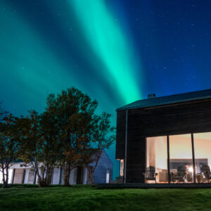 Turquoise aurora above a lit house at Skagenhaugen, Bø i Vesterålen