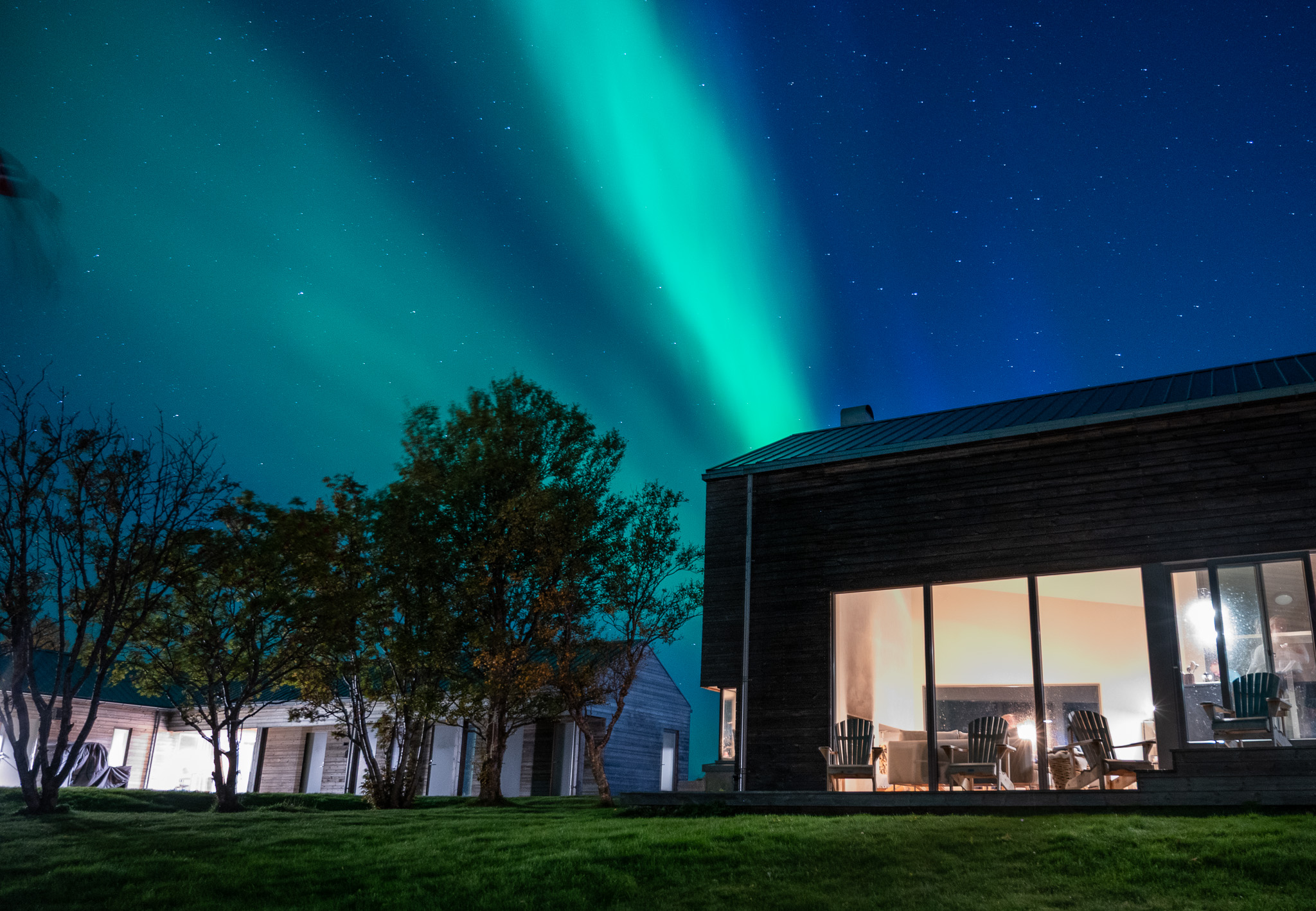 Turquoise aurora above a lit house at Skagenhaugen, Bø i Vesterålen