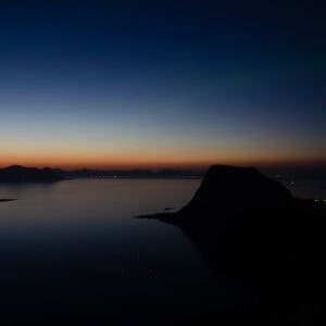 A dark headland reaching into a mirror-calm sea at blue hour
