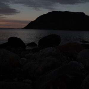 Weathered boulders on a shoreline with an island resting in dusk light