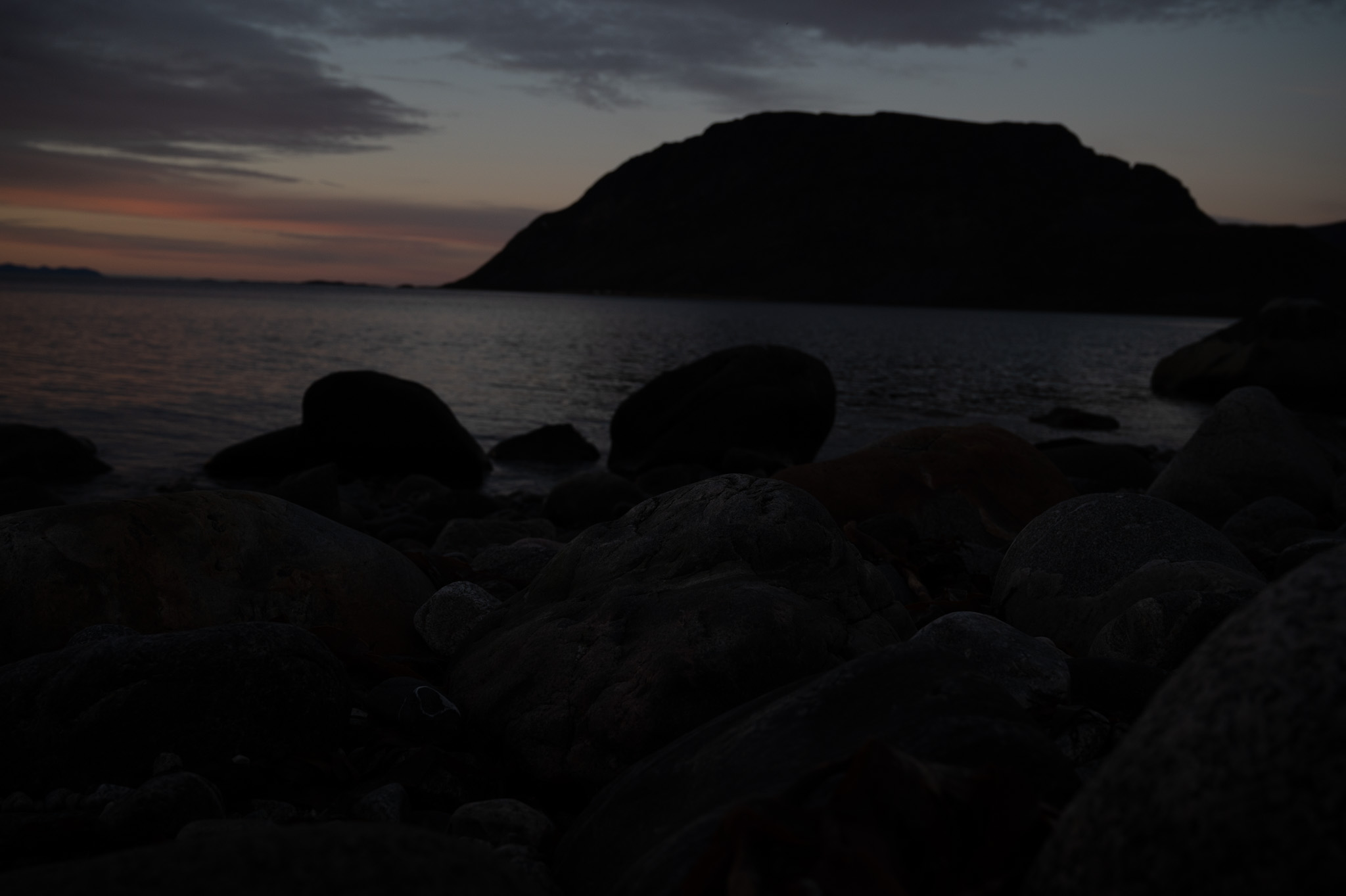 Weathered boulders on a shoreline with an island resting in dusk light
