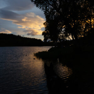 Clouds catching last light above a dark forest lake