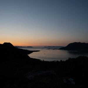 Orange horizon fading over a dark fjord seen from a hillside
