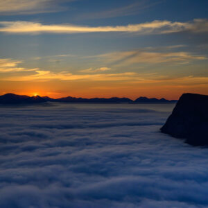 A single peak breaking through a sea of cloud at sunset