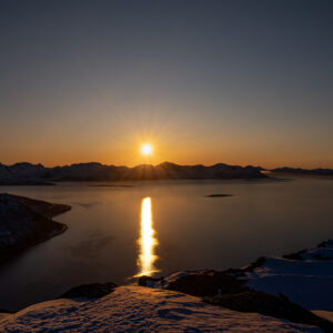 Low sun laying a column of light across a frozen arctic fjord