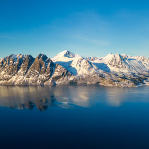 Snow-covered peaks reflected in a deep blue arctic fjord