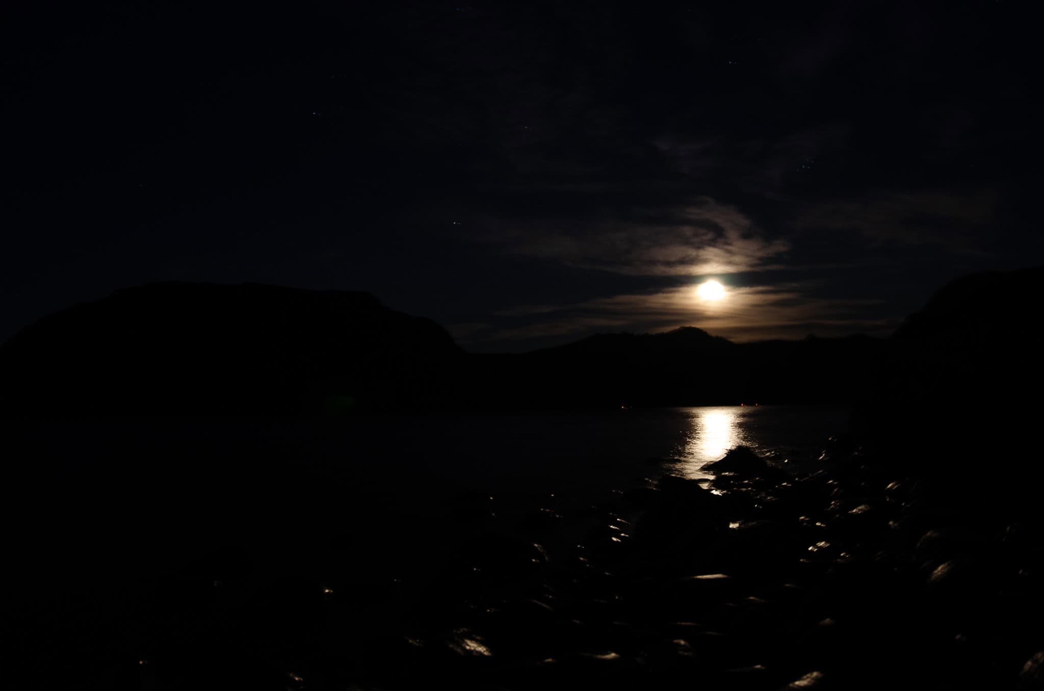 Full moon casting a silver path over a fjord with distant village lights
