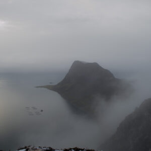 A mountain rising from fog with sun glowing on the water below