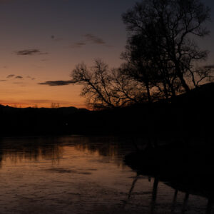 Warm evening sky reflected in a dark river beneath a wooded ridge