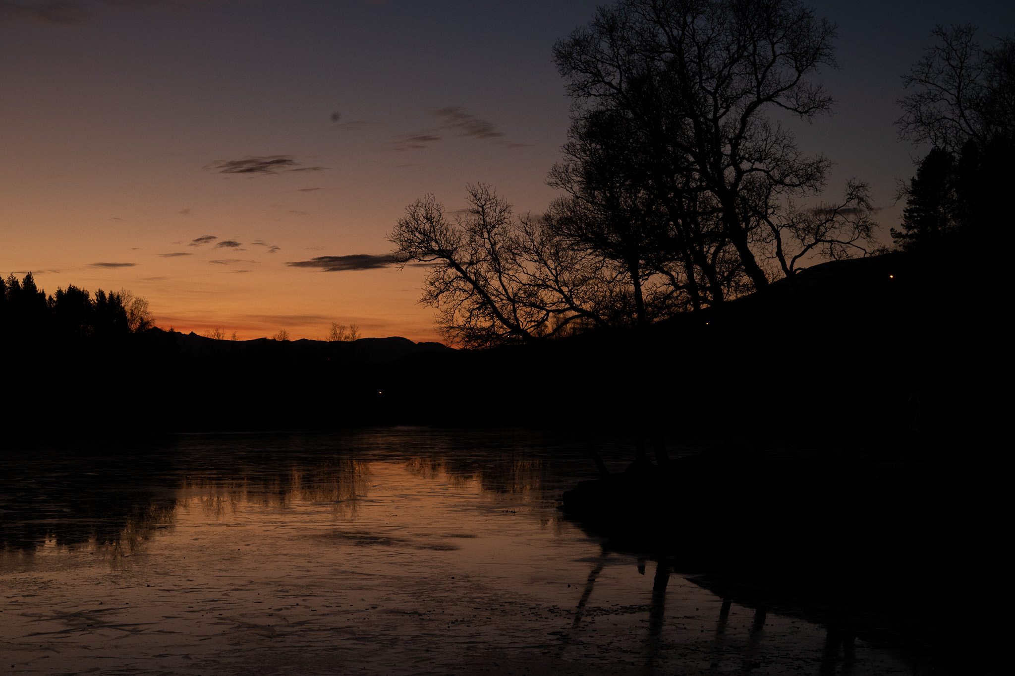 Warm evening sky reflected in a dark river beneath a wooded ridge