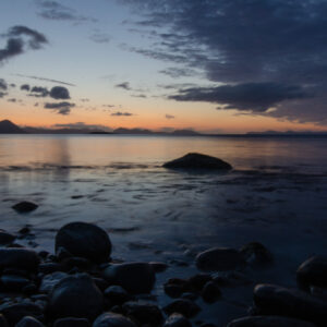 Rounded beach stones and calm water under a soft evening sky