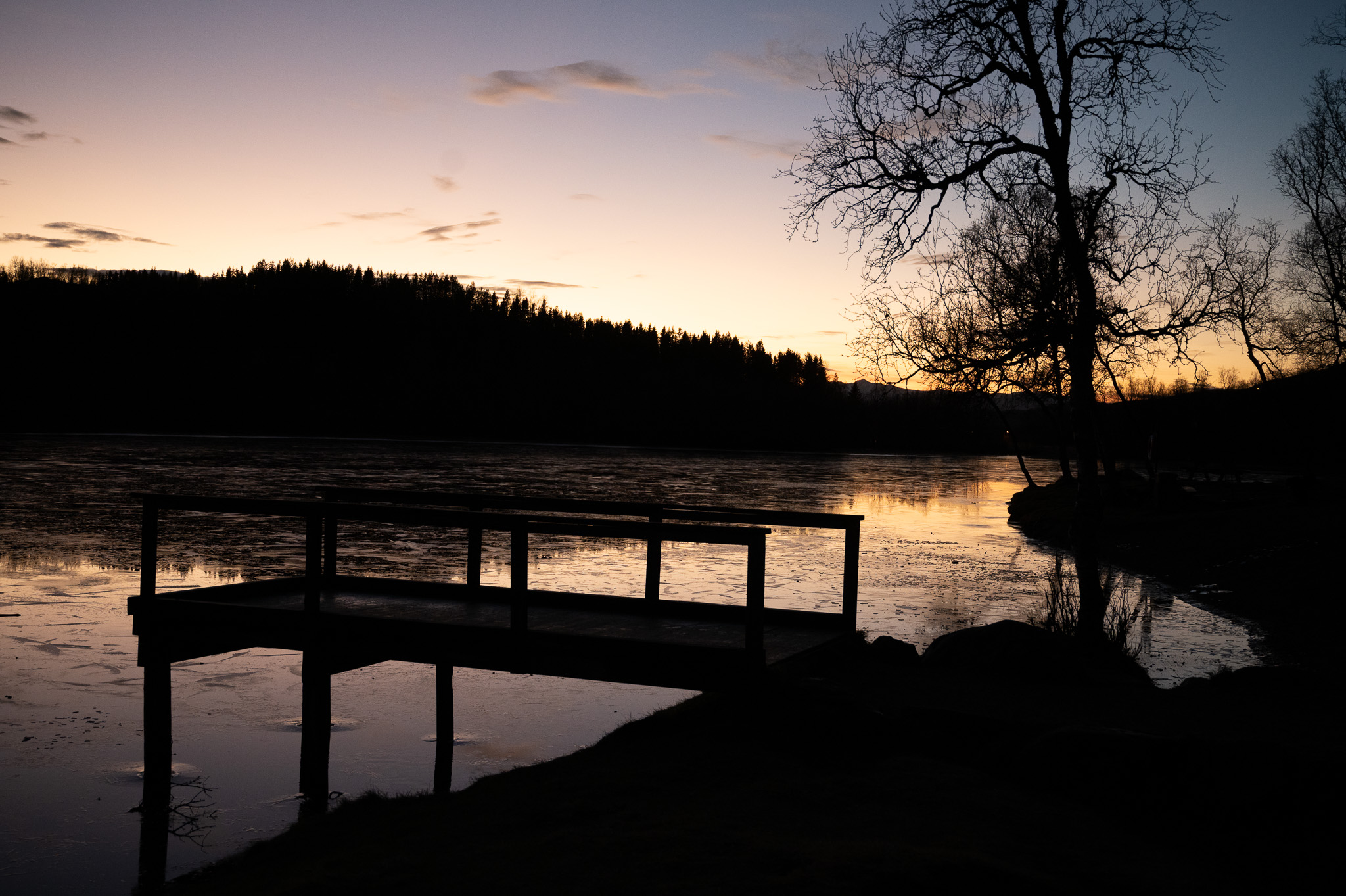 Wooden jetty reaching into a mirror-still lake under a fading sky