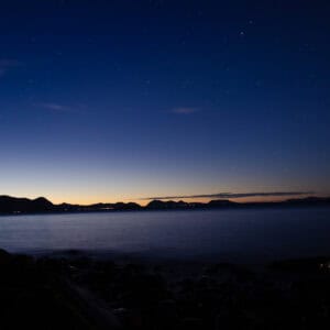 Coastal town lights under a deep blue twilight sky above the sea
