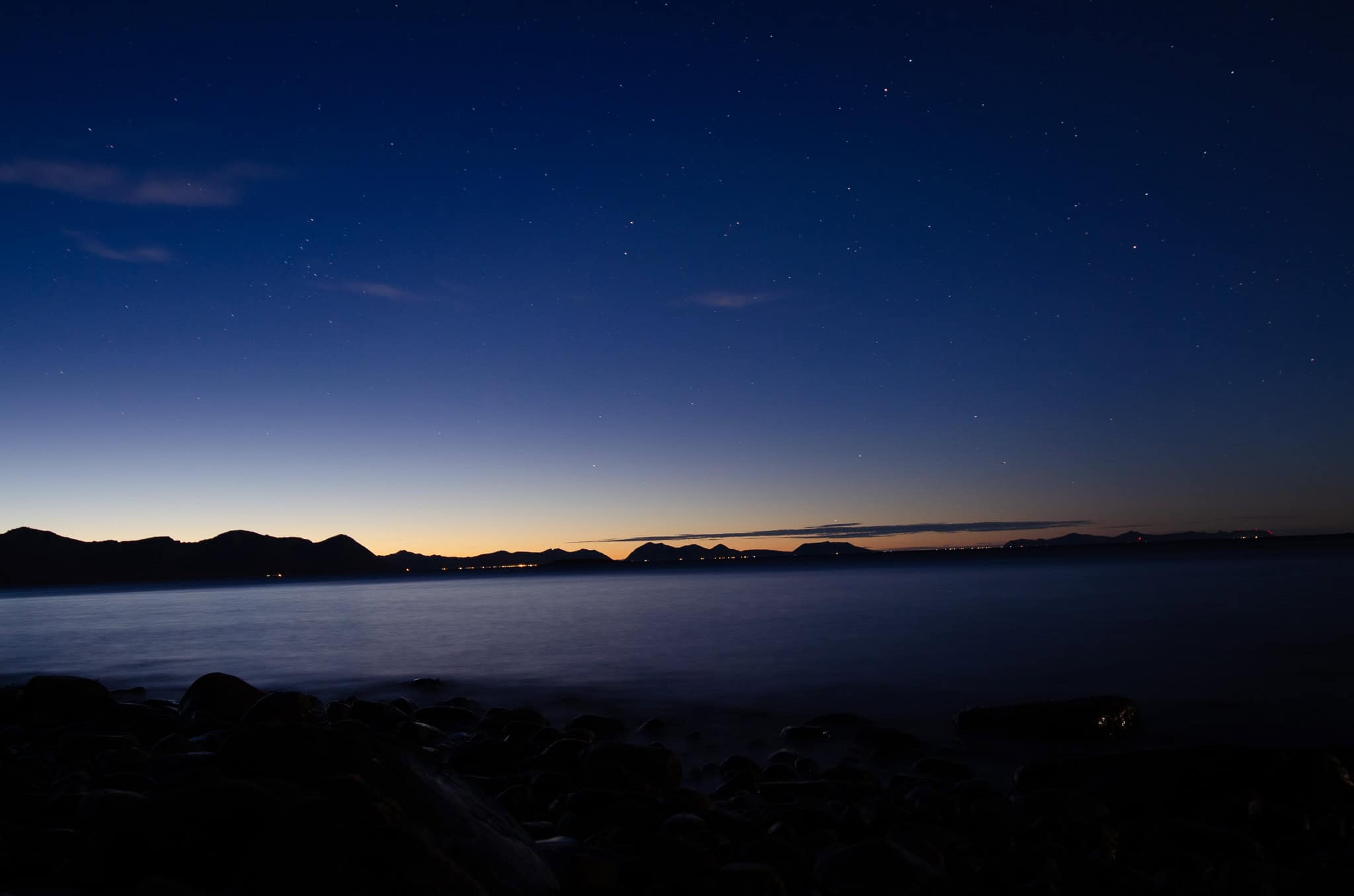 Coastal town lights under a deep blue twilight sky above the sea