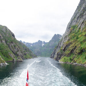 A ship's wake between the steep walls of a narrow Norwegian fjord